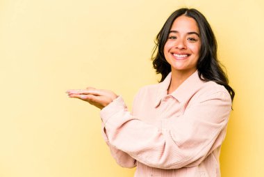 Sarı arka planda izole edilmiş genç İspanyol bir kadın. Elinde palmiyesinde bir kopya alanı var..