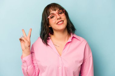 Mavi arka planda izole edilmiş genç beyaz kadın neşeli ve kaygısız parmakları olan bir barış sembolü gösteriyor..