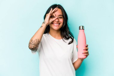Mavi arka planda termosu olan genç İspanyol kadın heyecanlı..