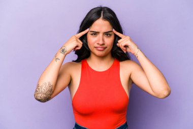 Mor arka planda izole edilmiş genç İspanyol kadın bir işe odaklanmış, işaret parmaklarını işaret ediyor..