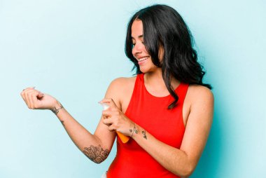 Mavi arka planda güneş kremi tutan genç İspanyol kadın.