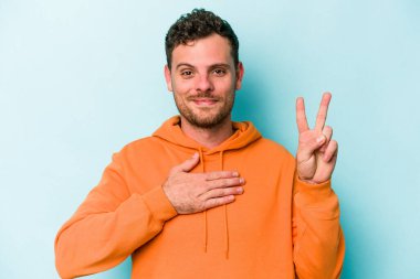 Kafkasyalı genç adam mavi arka planda izole edilmiş yemin ediyor, elini göğsüne koyuyor..