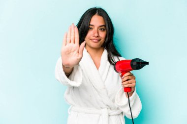 Mavi arka planda izole edilmiş kurutucuyu tutan genç İspanyol kadın elini uzatmış, dur işareti göstererek seni engelliyor..