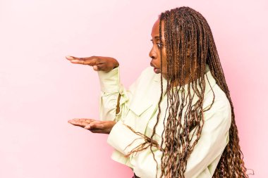 Pembe arka planda izole edilmiş genç Afrikalı Amerikalı kadın elleri arasında bir kopya alanı tutarken şok ve hayrete düştü..