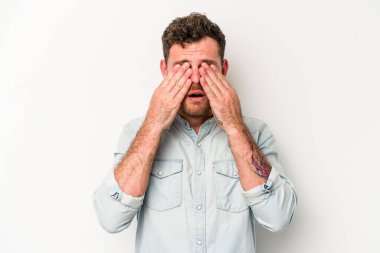 Beyaz arka planda izole edilmiş genç beyaz bir adam elleriyle gözlerini kapatmaktan korkuyor..