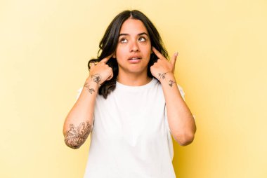 Sarı arka planda izole edilmiş, parmaklarıyla kulaklarını kapatan genç İspanyol kadın, gürültülü bir ortam yüzünden stresli ve çaresiz..