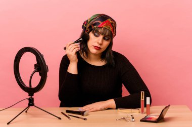 Makyaj sanatçısı genç bir kadın pembe arka planda özel bir makyaj dersi veriyor.