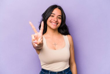 Mor arka planda izole edilmiş genç İspanyol kadın neşeli ve kaygısız parmakları olan bir barış sembolü gösteriyor..