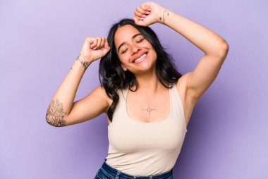 Mor arka planda izole edilmiş genç İspanyol kadın özel bir günü kutluyor, atlıyor ve enerjiyle kollarını kaldırıyor..