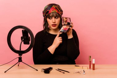 Makyaj sanatçısı genç bir kadın pembe arka planda özel bir makyaj dersi veriyor.