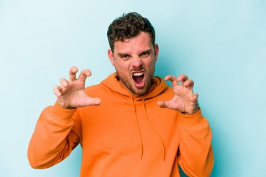 Mavi arka planda izole edilmiş genç beyaz adam pençelerini kedi taklidi yaparken gösteriyor, agresif bir hareket..