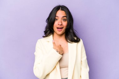 Mor arka planda izole edilmiş genç İspanyol kadın parmağını göstererek şaşırdı, geniş bir gülümsemeyle..