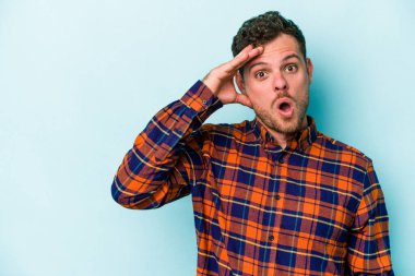 Mavi arka planda izole edilmiş genç beyaz adam yüksek sesle bağırıyor, gözleri açık ve elleri gergin tutuyor..