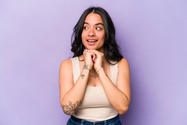 Mor arka planda izole edilmiş genç İspanyol kadın şans için dua ediyor, şaşırmış ve ön tarafa bakan ağzını açıyor..
