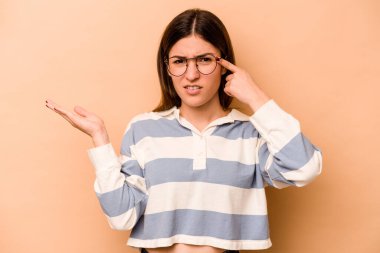 Latin kökenli genç bir kadın bej arka planda izole edilmiş ve elinde bir ürün tutuyor..