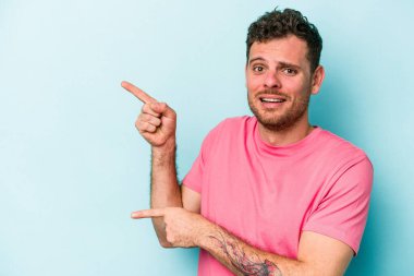 Mavi arka planda izole edilmiş genç beyaz adam işaret parmağıyla fotokopi alanını işaret ederek şok oldu..