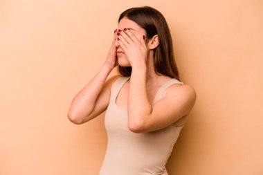 Latin kökenli genç bir kadın bej arka planda izole edilmiş, elleriyle gözlerini kapatmaktan korkuyor..