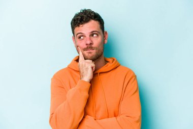 Kafkasyalı genç bir adam mavi arka planda izole edilmiş. Bir strateji planlıyor, bir iş yolu düşünüyor..