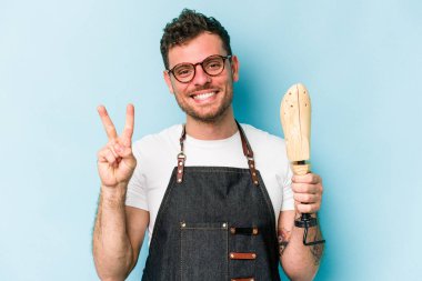 Kafkasyalı genç kunduracı, mavi arka planda iki numarayı parmaklarıyla gösteriyor..