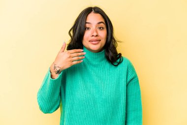 Sarı arka planda izole edilmiş genç İspanyol kadın bir şeye gülüyor, elleriyle ağzını kapatıyor..