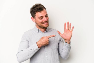 Beyaz arka planda izole edilmiş genç beyaz bir adam gülümseyerek beş numarayı parmaklarıyla gösteriyor..