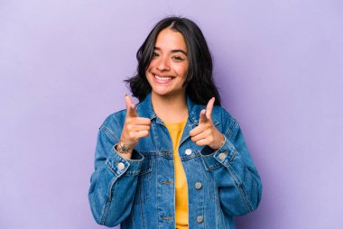 Mor arka planda izole edilmiş genç İspanyol kadın parmaklarıyla ön tarafı işaret ediyor..