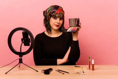 Makyaj sanatçısı genç bir kadın pembe arka planda özel bir makyaj dersi veriyor.