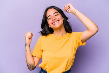 Mor arka planda izole edilmiş genç İspanyol kadın özel bir günü kutluyor, atlıyor ve enerjiyle kollarını kaldırıyor..