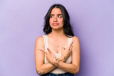 Mor arka plan noktalarında izole edilmiş genç İspanyol kadın iki seçenek arasında seçim yapmaya çalışıyor..