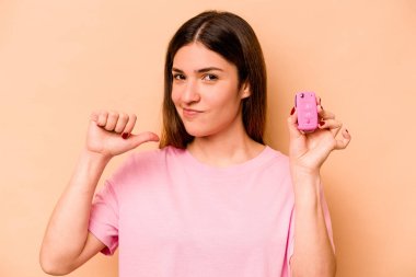 Latin kökenli genç bir kadın bej arka planda izole edilmiş bir araba tutuyor gururlu ve kendinden emin hissediyor, örnek olarak..