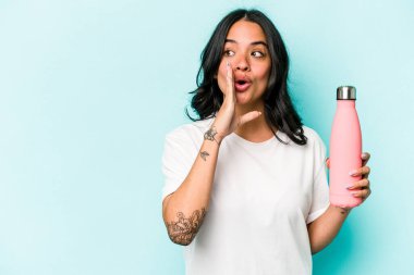 Mavi arka planda termosu olan Latin kökenli genç bir kadın gizli bir sıcak fren haberi veriyor ve yana bakıyor.