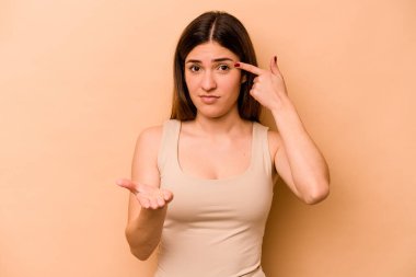 Latin kökenli genç bir kadın bej arka planda izole edilmiş ve elinde bir ürün tutuyor..