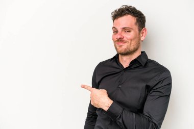Beyaz arka planda izole edilmiş genç beyaz bir adam gülümsüyor ve boş alanda bir şeyler gösteriyor..