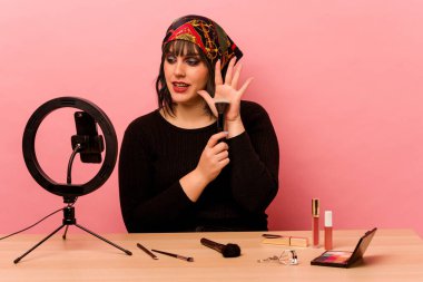 Makyaj sanatçısı genç bir kadın pembe arka planda özel bir makyaj dersi veriyor.