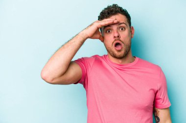 Kafkasyalı genç adam mavi arka planda izole edilmiş, uzaklara bakıyor ve elini alnına koyuyor..