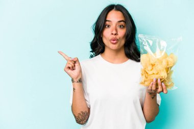 Mavi arka planda izole edilmiş bir paket cipsi tutan genç İspanyol kadın...
