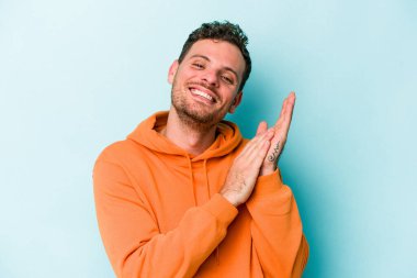 Kafkasyalı genç adam mavi arka planda izole edilmiş enerjik ve rahat hissediyor, ellerini ovuşturuyor kendinden emin.