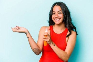 Mavi arka planda güneş kremi tutan genç İspanyol kadın.