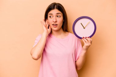 Elinde bej arka planda izole edilmiş bir saat tutan genç İspanyol kadın bir dedikoduyu dinlemeye çalışıyor..