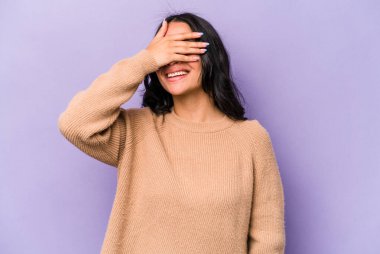 Mor arka planda izole edilmiş genç İspanyol kadın elleriyle gözlerini kapatıyor, geniş bir gülümsemeyle bir sürpriz bekliyor..