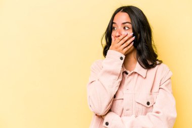 Genç İspanyol kadın sarı arka planda izole edilmiş. Düşünceli bir şekilde bir fotokopi odasına bakıyor. Ağzını eliyle kapatıyor..