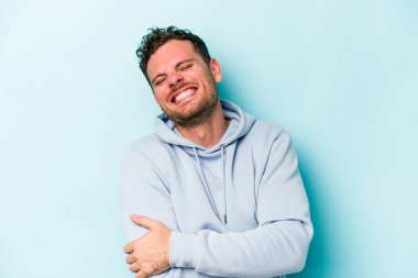 Kafkasyalı genç adam mavi arka planda izole edilmiş gülüyor ve eğleniyor..