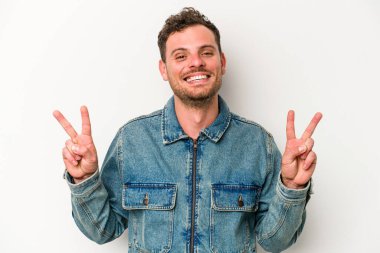 Beyaz arka planda izole edilmiş genç beyaz bir adam zafer işareti gösteriyor ve gülümsüyor..