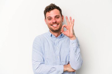 Beyaz arka planda izole edilmiş genç beyaz bir adam bir göz kırptı ve elleriyle iyi bir jest yaptı..