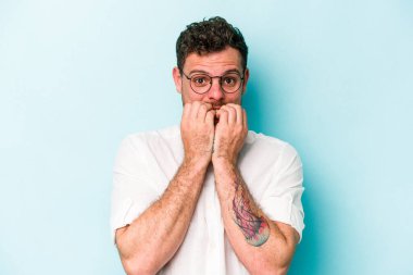 Mavi arka planda izole edilmiş, tırnak yiyen, gergin ve endişeli genç bir beyaz adam..