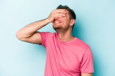 Mavi arka planda izole edilmiş genç beyaz adam ellerini başının üstünde tutarak neşe içinde gülüyor. Mutluluk kavramı.