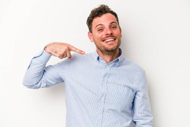 Beyaz arka planda yaşayan beyaz tenli genç bir adam gömlek fotokopi alanını gösteriyor, gururlu ve kendinden emin.