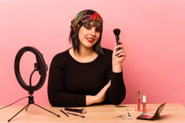 Makyaj öğretmeni olan genç bir kadın pembe arka planda izole edilmiş mutlu, güler yüzlü ve neşeli..