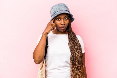 Genç Afrikalı Amerikalı bir kadın pembe arka planda izole edilmiş bir şekilde sahile gidiyor. Parmağıyla tapınağı işaret ediyor, düşünüyor ve bir göreve odaklanıyor..