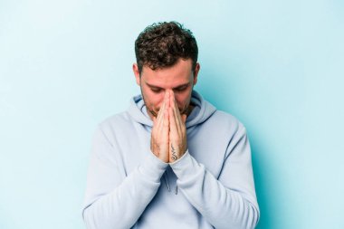 Kafkasyalı genç adam mavi arka planda izole edilmiş dua ediyor, bağlılık gösteriyor, dindar biri ilahi ilham arıyor..